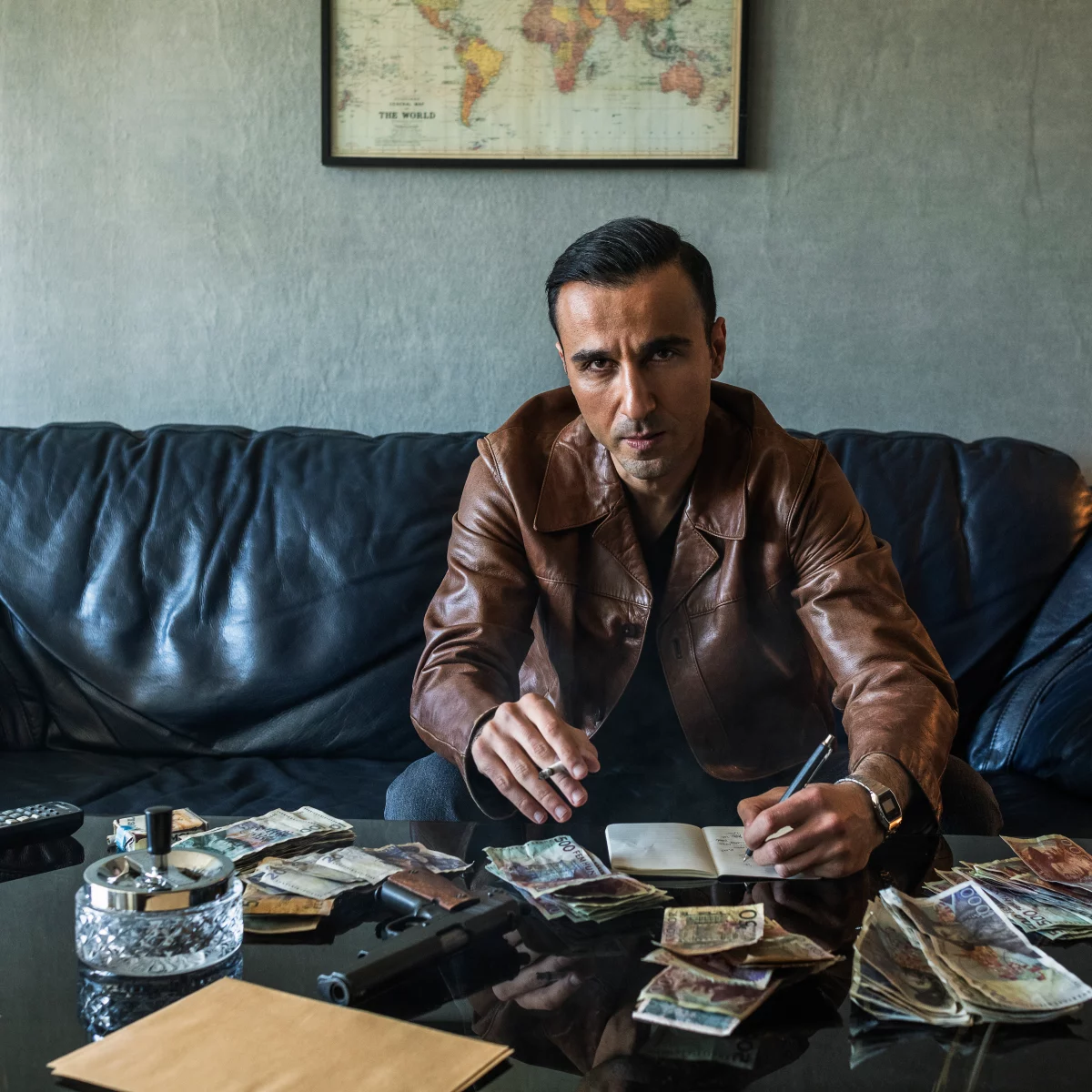 Middle aged man in leather jacket sitting at a table with money and a notebook.